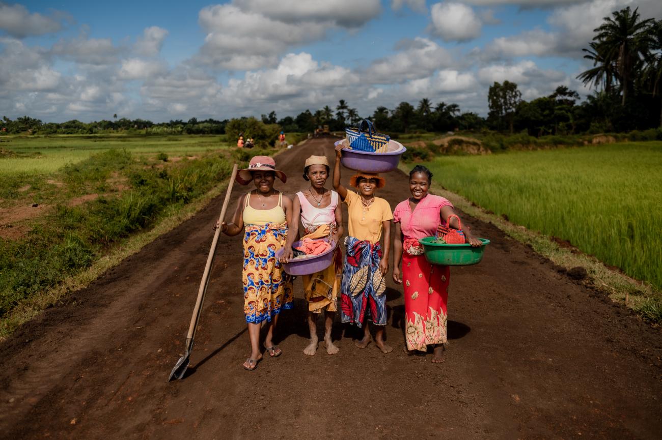 Quatre femmes en Lambahoany sur une route tenant dans leurs main des cuvettes